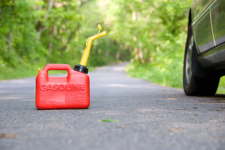 A red plastic gas can sitting in the middle of a country road next to a car.の写真素材
