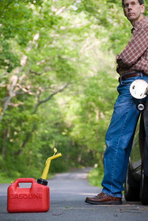 Upset man leaning against his car on a country road, staring down the road with an empty gas can at his feet.  Focus is on the gas can in the foreground.の写真素材