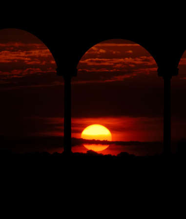 A brilliant russet sunset is the backdrop for a silhouette of a gazebo.の写真素材