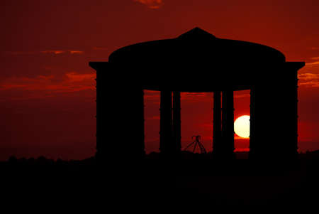 A spectacular deep russet sunset glows behind a silhouette of a gazebo.の写真素材