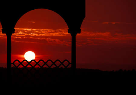 The sun sets in brilliant shades of red and orange and places the gazebo in silhouette.の写真素材