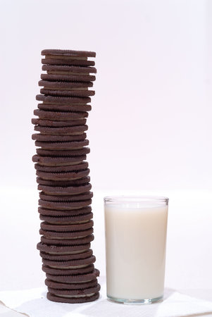 Chocolate Cookies and Milk - Chocolate frosting-filled cookies stacked high on a napkin alongside a glass of cold milk.の写真素材