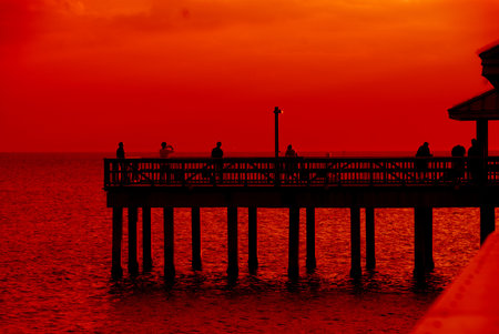 Sunset, Gulf of Mexico - A brilliant red and orange sunset over the water of the Gulf of Mexico at Ft Meyers Beach in December, watched by people standing on the pier.の写真素材