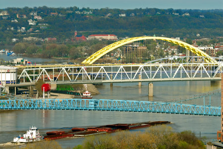 River Barge - A barge pushes up river maneuvering under the many colorful bridges spanning the Ohio River between the cities of Cincinnati Ohio and Covington Kentucky. の写真素材