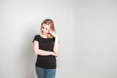 Young woman in black t-shirt holding head in pain against gray backgroundの写真素材