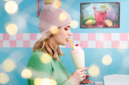 Portrait of a lovely girl in green sweater with bokeh lights. Pretty blonde girl with a milkshake