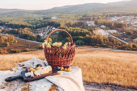 Picnic in the countryside. Napkin, cheese brie and plums on a wooden board. Basket with flowerの写真素材