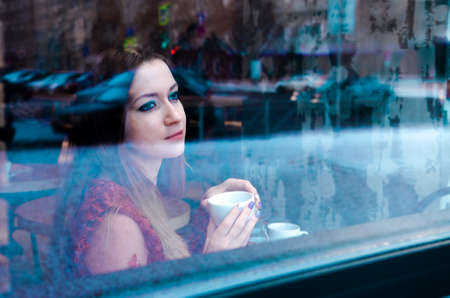 Portrait of young woman drinking tea and looking out of the coffee shop window. Business lunch in...