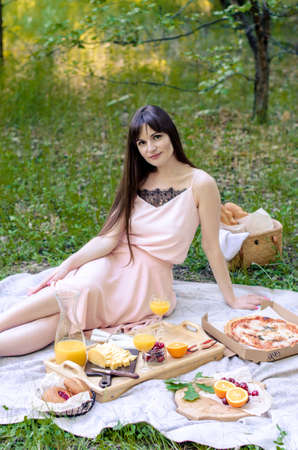 Beautiful young woman having picnic on sunny spring day. Picnic setting on the grass with basket, bread, cheese and fruitの写真素材