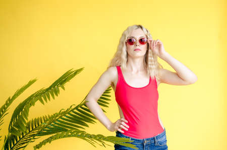 A beautiful young girl wearing red sunglasses stands near a yellow background. Palm leafの写真素材
