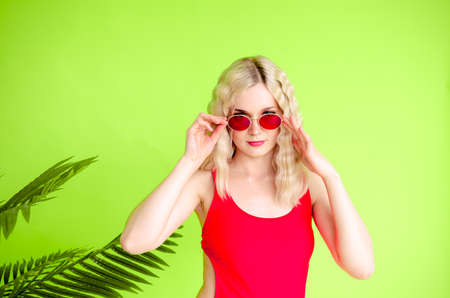 A beautiful young girl wearing red sunglasses stands near a green background. Palm leafの写真素材