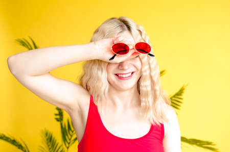 A beautiful young girl with red sunglasses stands near a yellow background with palm leafの写真素材