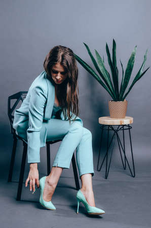 Young woman trying on elegant shoes with high heels. Grey background in studio. Total look. Copyspaceの写真素材