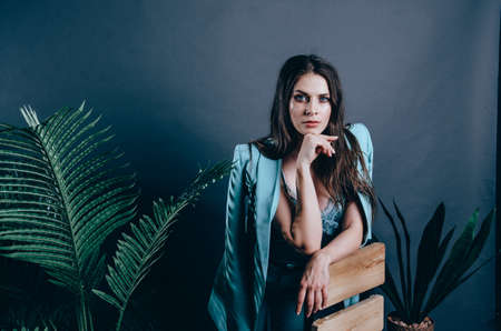 Young female business coach. Portrait of young woman in blue suit on background with plants. Studio...