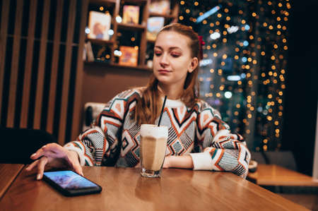 Young redhead woman in a cafe with a cup of coffee. Casual portrait of hipster girl. Bokeh...