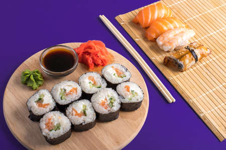 Sushi set sashimi with salmon, shrimp, eel and sushi rolls served on bamboo mat and wooden board. Violet background. Japanese menuの写真素材
