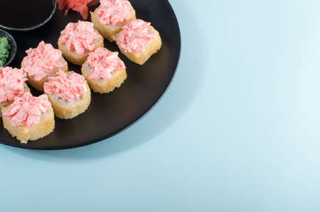 Sushi rolls set with red mayonnaise sauce served on black plate. Pink and blue backgroundの写真素材
