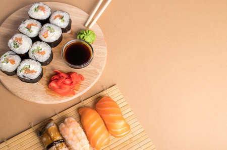 Sushi set uramaki and rolls served on bamboo mat and wooden board on a light beige background. Copy spaceの写真素材