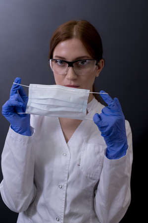 Female doctor in a white coat showing face mask or medical mask to protection from coronavirusの写真素材