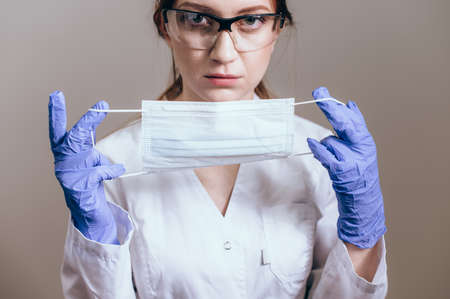 Female doctor in a white coat showing face mask or medical mask to protection from coronavirusの写真素材