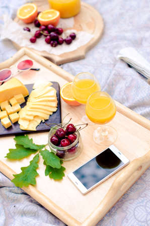 Picnic setting on the grass. Cheese, orange juice, sweet cherry, mobile phone
