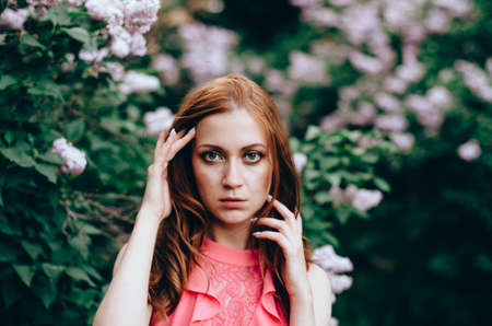 Attractive young woman with perfect red long hairs in a garden with lilacsの写真素材