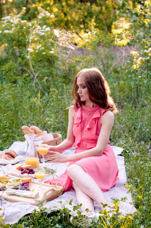 Portrait of romantic young woman in pink dress having summer picnic in parkの写真素材