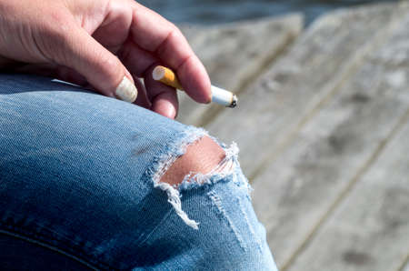 woman in torned jeans smoking a cigaretteの写真素材
