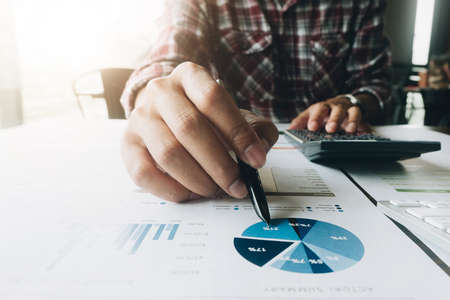 Close up of businessman or accountant hand holding pen working on calculator to calculate business...