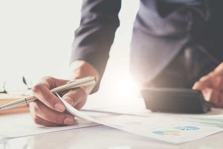 Close up of businessman or accountant hand holding pen working on calculator to calculate business data, accountancy document and laptop computer at office, business conceptの写真素材