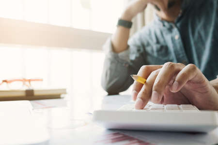 Close up of businessman or accountant hand holding pen working on calculator to calculate business...