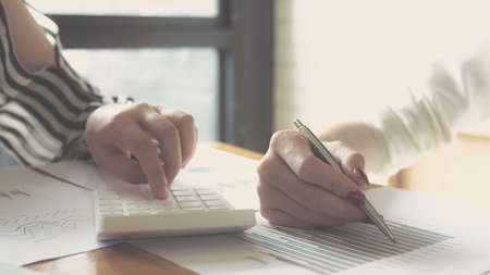 Close up Two  Businesswoman using calculator and point graph for do math finance on wooden desk in office and business working background, tax, accounting, statistics and analytic research conceptの写真素材