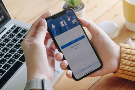 CHIANG MAI, THAILAND - JUN 7, 2020: Facebook social media app logo on log-in, sign-up registration page on mobile app screen on iPhone X (10) in person's hand working on e-commerce shopping businessのeditorial素材