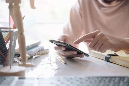 Close up hand of woman holding smartphone and using laptop computer at home. Online shopping concept