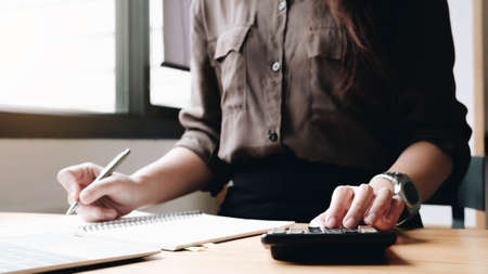 Close up Businesswoman using calculator and laptop for do math finance on wooden desk in office and business working background, tax, accounting, statistics and analytic research conceptの写真素材