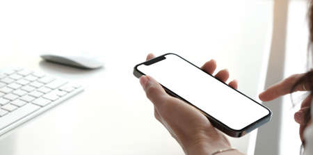Mockup image blank white screen cell phone.women hand holding texting using mobile on desk at home...