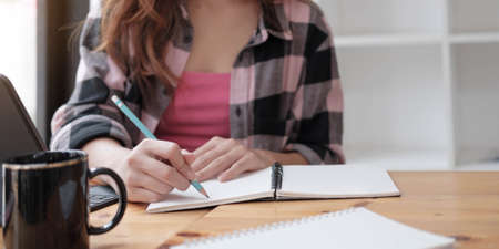 Close up of a woman writer hand writing in a notebook at home.の写真素材