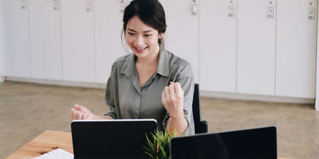 Portrait of happy young successful businesswoman celebrate something with arms up. Happy woman sit at office and look at laptop.の写真素材