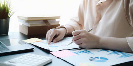 woman checking paperwork from accounting department to analyse number on document, using laptop...
