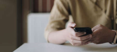 Mockup image of a woman holding mobile phone with blank black screen in cafe