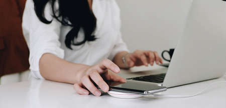 Cropped image of an office woman is charging a smartphone with a wireless charger while typing on a computer laptop.の写真素材