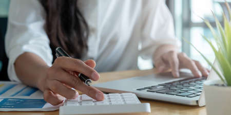 Close up Businesswoman using calculator and laptop for do math finance on wooden desk in office and...