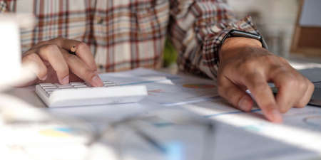 Businessman hands holding pen working on calculator and financial paperwork.
