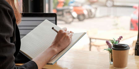 Crop close up of woman study online distant on laptop make note write in notebook sitting on desk at...