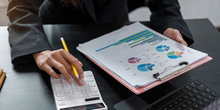 Woman with financial report and calculator. Woman using calculator to calculate report at the table...