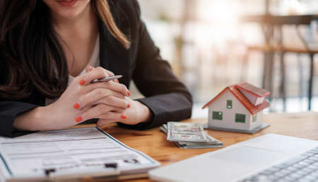 Cropped image of real estate agent assisting client to sign contract paper at desk with house modelの写真素材