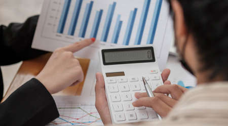 Close up Businessman and partner using calculator and point report for calaulating finance, tax,...