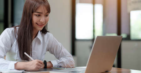 Online education concept. Serious female student studying, watching webinar, taking notes in...