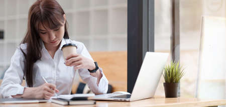Online education concept. Serious female student studying, watching webinar, taking notes in...