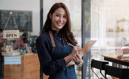 Portrait of a smiling Asian entrepreneur standing behind her cafe counter with open sign boardの写真素材